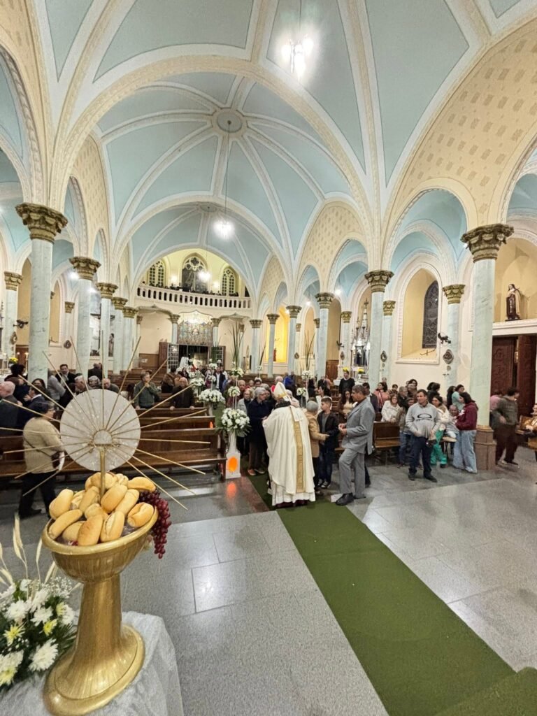 Interior da Igreja Matriz de Brazópolis com abóbadas azul-claras, colunas de capitéis dourados e coro ao fundo, durante missa com bispo