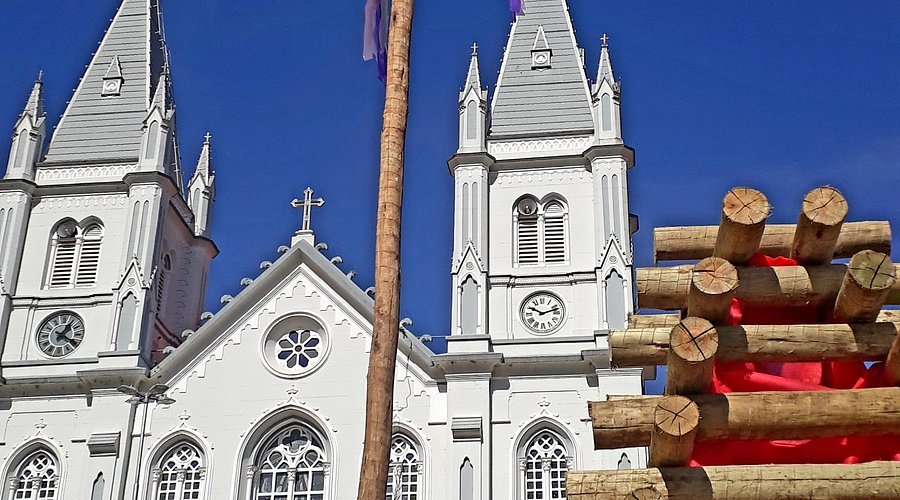 Torres da Igreja Matriz de São Caetano em Brazópolis com relógios, ao lado de mastro e fogueira de toras montados para festa